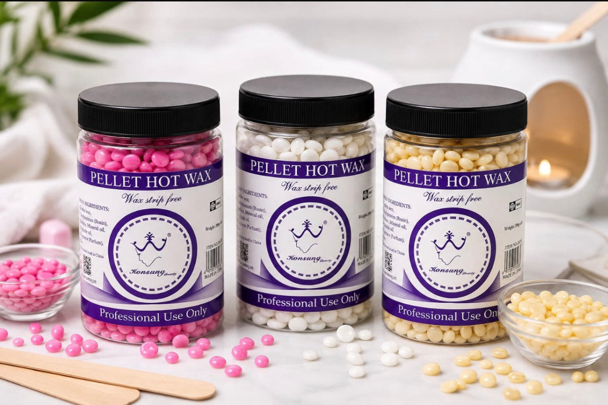 Three jars of Kemonette Pellet Hot Wax in pink, white, and yellow, arranged on a white surface with small bowls of the wax pellets and wooden spatulas.