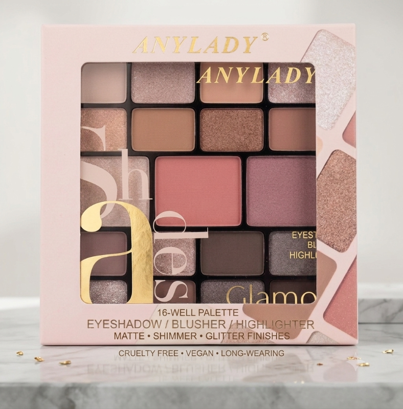 Anylady Glamo 16-well eyeshadow palette in a light pink box with gold lettering, displayed on a marble surface with small gold leaf accents.