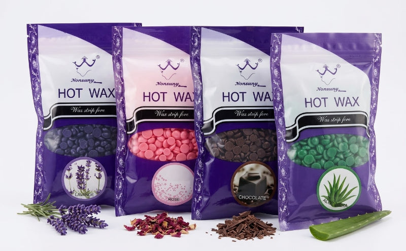 Four stand-up pouches of Nononsense Hot Wax in purple packaging, arranged in a row with botanical ingredients in front: lavender, rose petals, chocolate pieces, and aloe vera. The packages show different wax colors visible through clear windows: dark purple, pink, brown, and green.