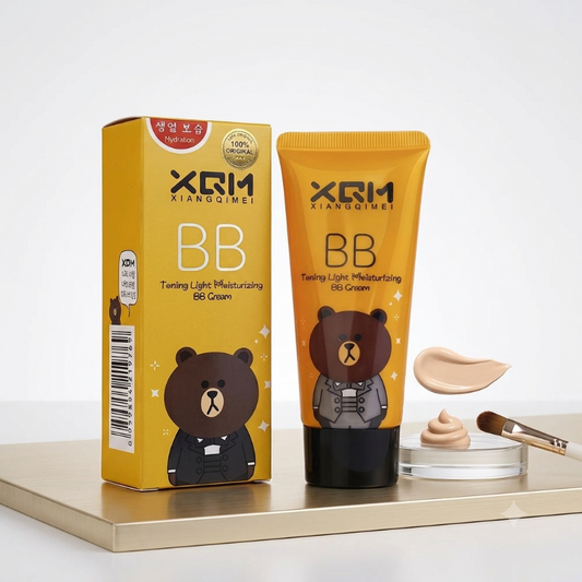 XRM Xiangqimei BB Cream in a yellow squeeze tube and matching box, featuring a cartoon bear illustration, displayed on a gold tray with a dollop of cream and a makeup brush against a white background.